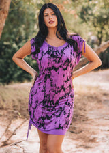 Woman wearing a purple and black tie-dye dress outdoors.