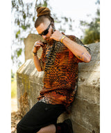 Man wearing a patterned shirt leaning against a stone wall outdoors