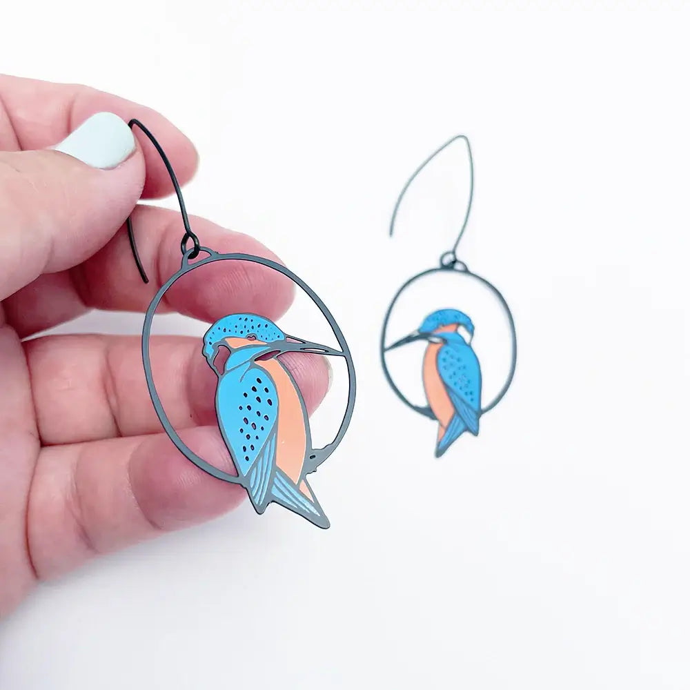 Earrings with bird design held by a hand on a white background