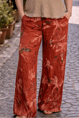 Woman standing on a street wearing a beige top and red patterned pants.
