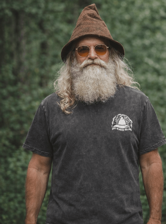 Man wearing a black t-shirt with a gnome graphic and text, standing against a green forest background.
