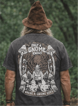 Man wearing a black t-shirt with a gnome graphic and text, standing against a green forest background.