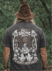 Man wearing a black t-shirt with a gnome graphic and text, standing against a green forest background.