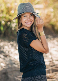 Woman wearing a navy blue patterned top and a striped hat outdoors.