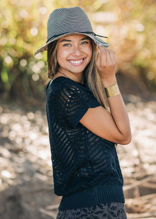 Woman wearing a navy blue patterned top and a striped hat outdoors.
