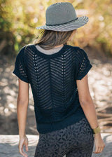 Person wearing a black knit top and patterned hat with a blurred natural background