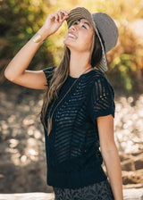 Woman wearing a black knit top and straw hat outdoors with a blurred natural background