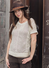 Woman wearing a beige knitted top and brown hat against a wooden wall.
