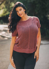Woman wearing a pink knitted top with a blurred natural background
