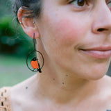 Close-up of a person wearing a bird-shaped earring with an orange and black design.