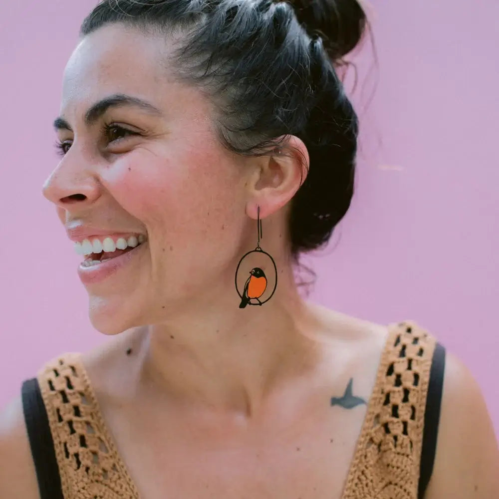 Woman wearing a unique earring with a bird design against a pink background