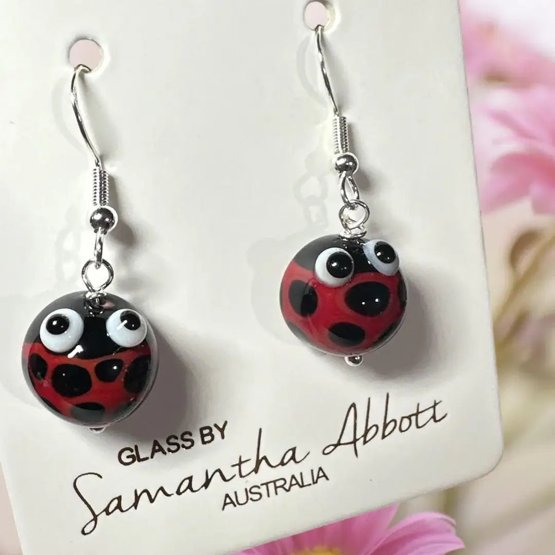 Pair of ladybug-themed earrings on a branded card with 'Glass by Samantha Abbott Australia' text.