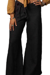 Woman wearing a mustard yellow top and black pants against a dark textured wall.