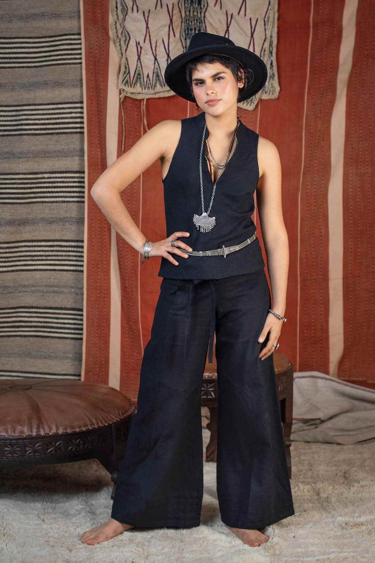 Person wearing a black sleeveless top and wide-leg pants in a room with patterned walls.