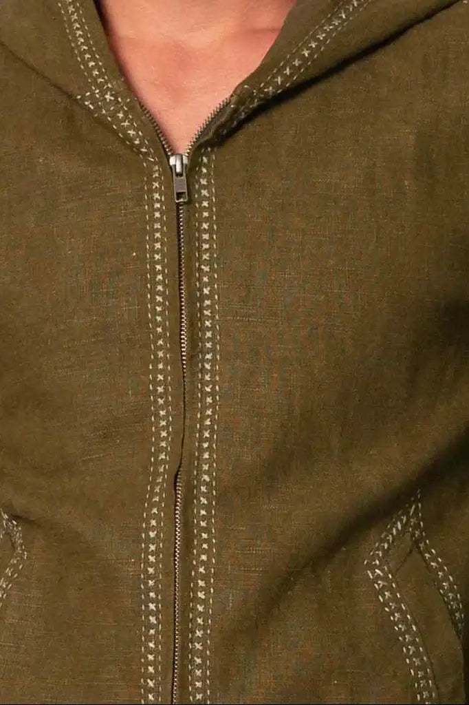 Close-up of an olive green zip-up hoodie with decorative contrast stitching along the zipper and pocket edges, worn by a model.