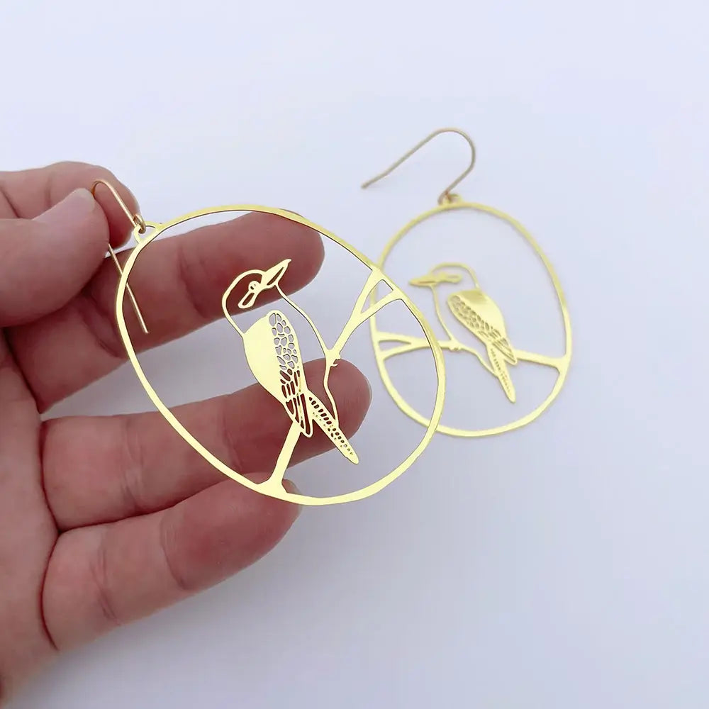 Gold bird-shaped earrings held by a hand on a white background