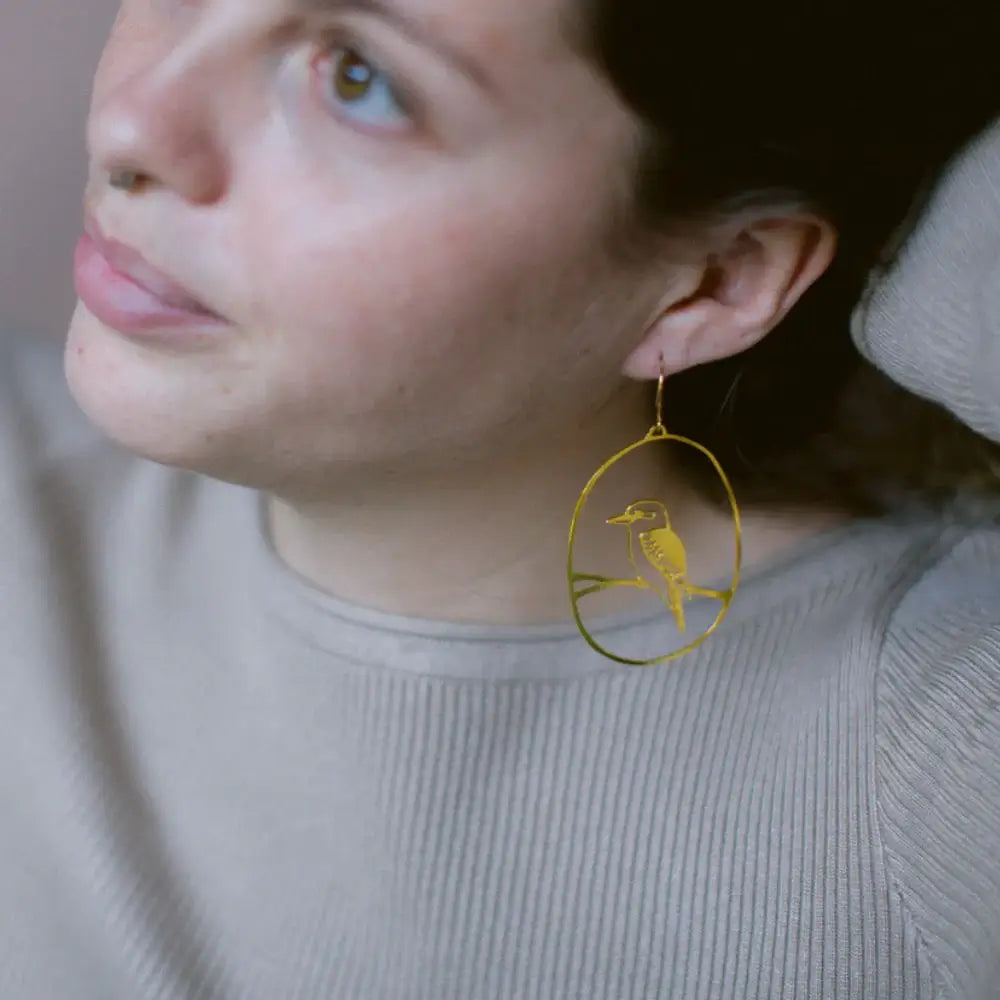 Close-up of a person wearing gold earrings with a bird design.