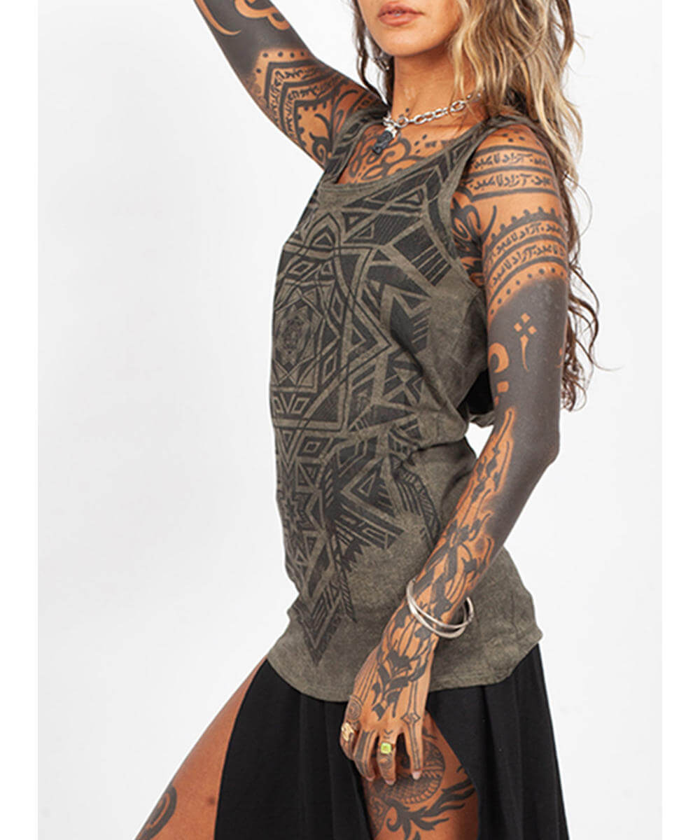 Person wearing a patterned top with tattoos on arms and hands against a white background