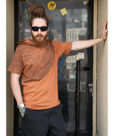 Man with dreadlocks wearing sunglasses and an orange shirt leaning against a door.