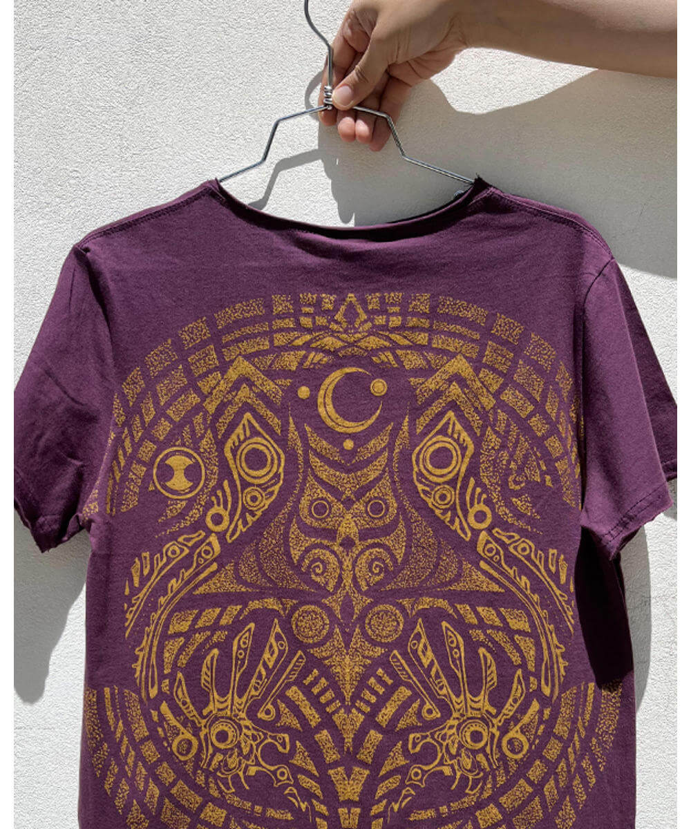Purple t-shirt with gold elephant design on a hanger against a light background