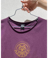 Purple t-shirt with a gold owl design on a hanger against a light gray background