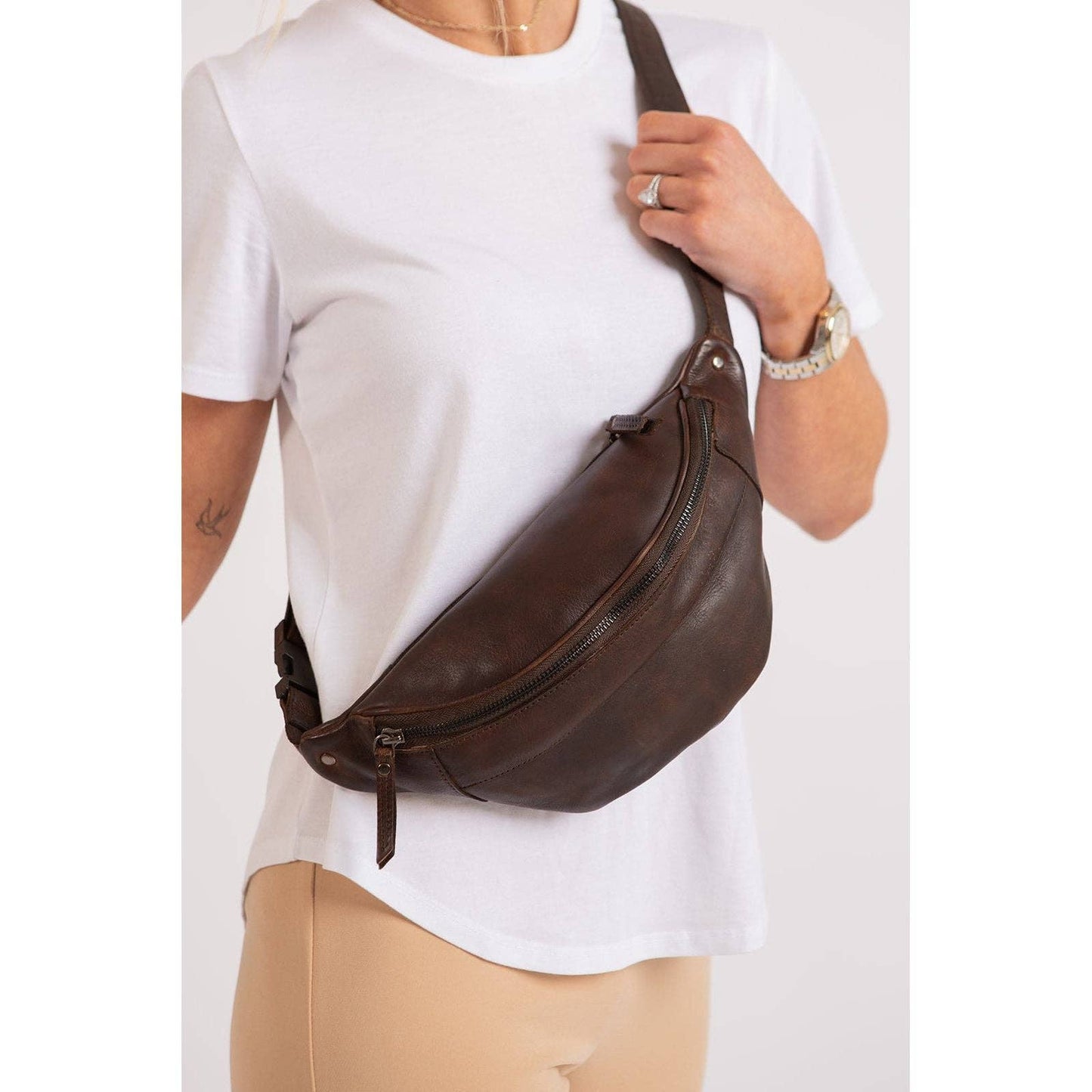 Person wearing a brown leather waist bag on a white background