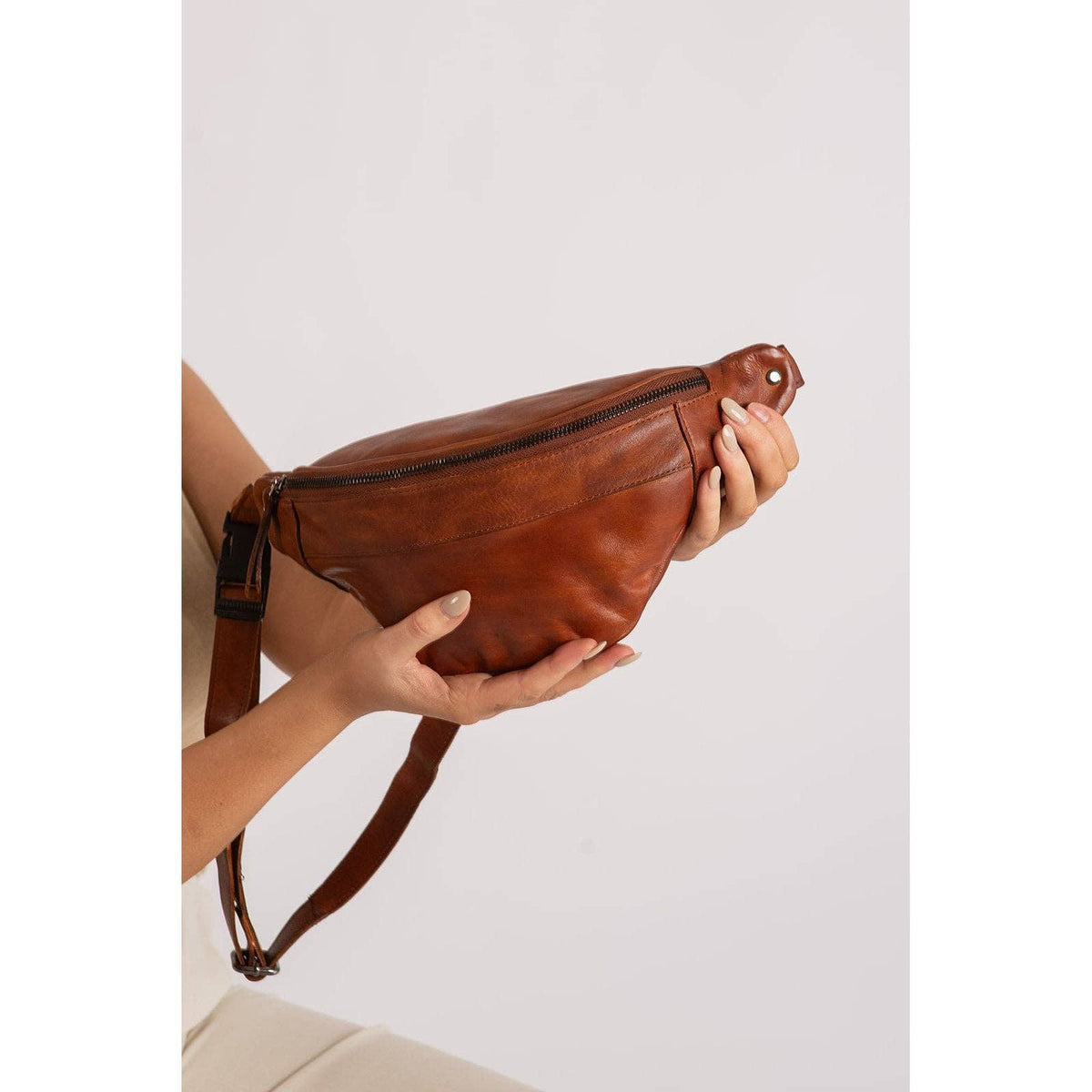 Brown leather waist bag held by a person against a light background