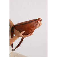 Brown leather waist bag held by a person against a light background