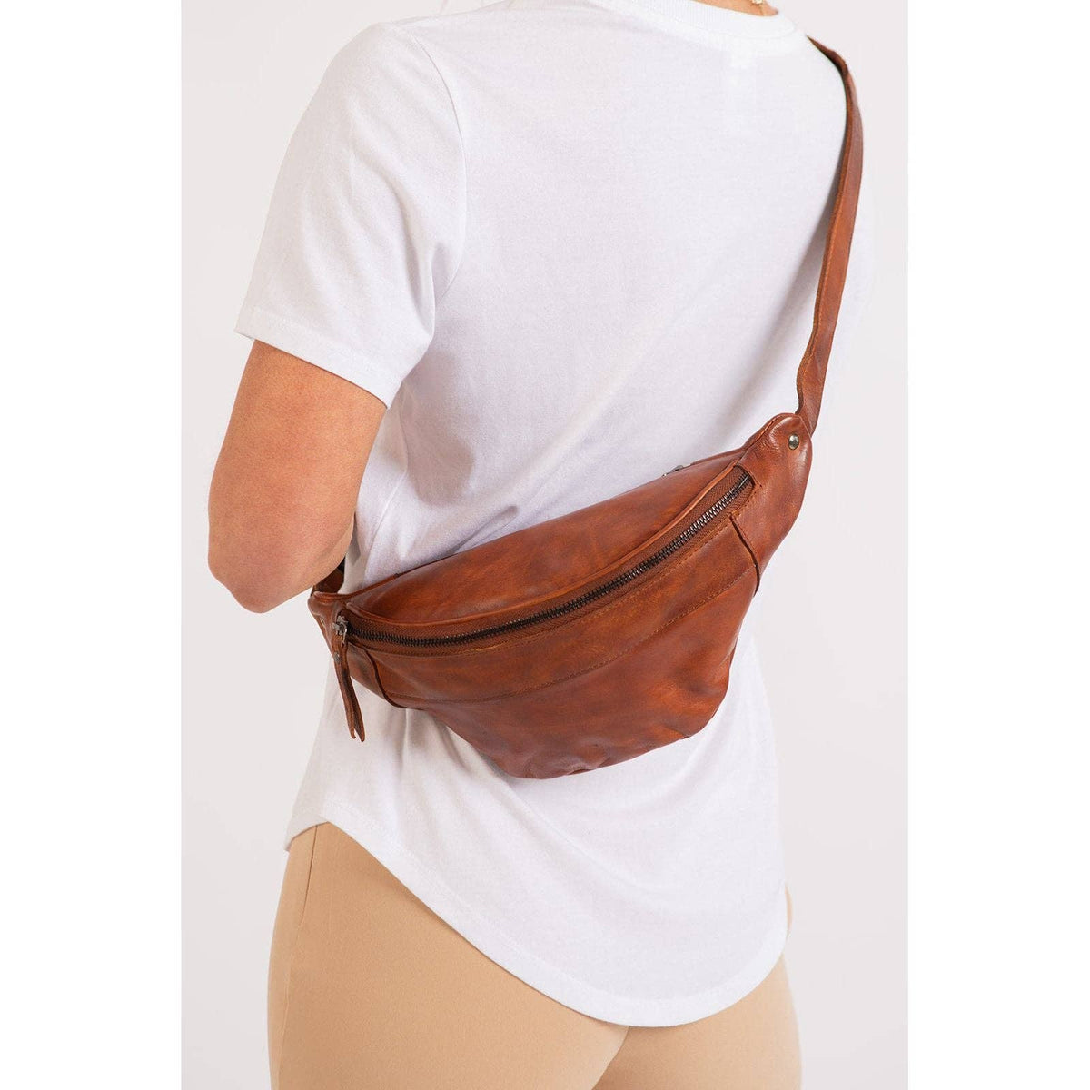 Person wearing a brown leather bag over one shoulder on a white background
