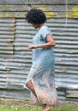 Woman wearing a blue dress standing in front of a corrugated metal wall.