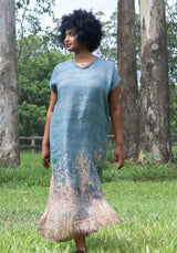 Woman wearing a blue dress with a textured pattern standing in a natural setting.