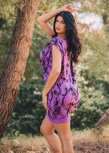 Woman in a purple tie-dye dress standing outdoors with trees in the background