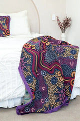 Colorful patterned blanket draped over a bed with white bedding.