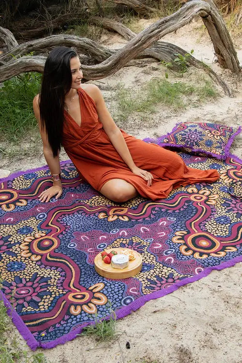 Woman in an orange dress sitting on a colorful patterned blanket outdoors.