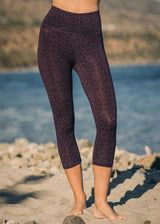 Person wearing dark patterned leggings standing on a beach with water in the background