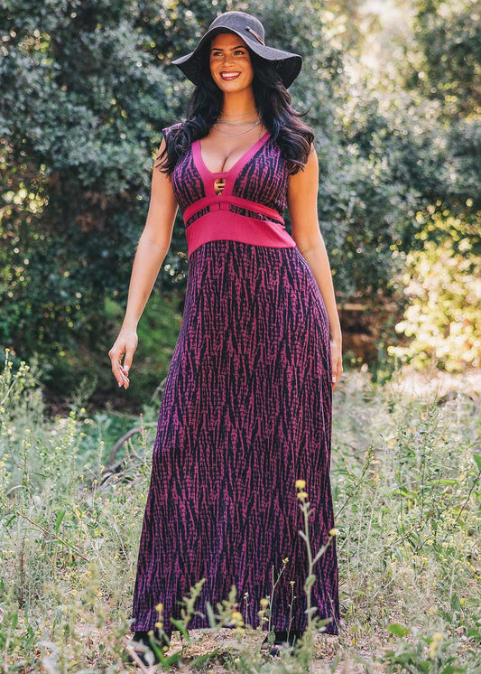 Woman in a purple and pink dress standing in a natural setting with greenery.