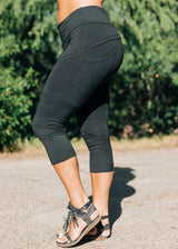 Person wearing black capri leggings with a blurred green background