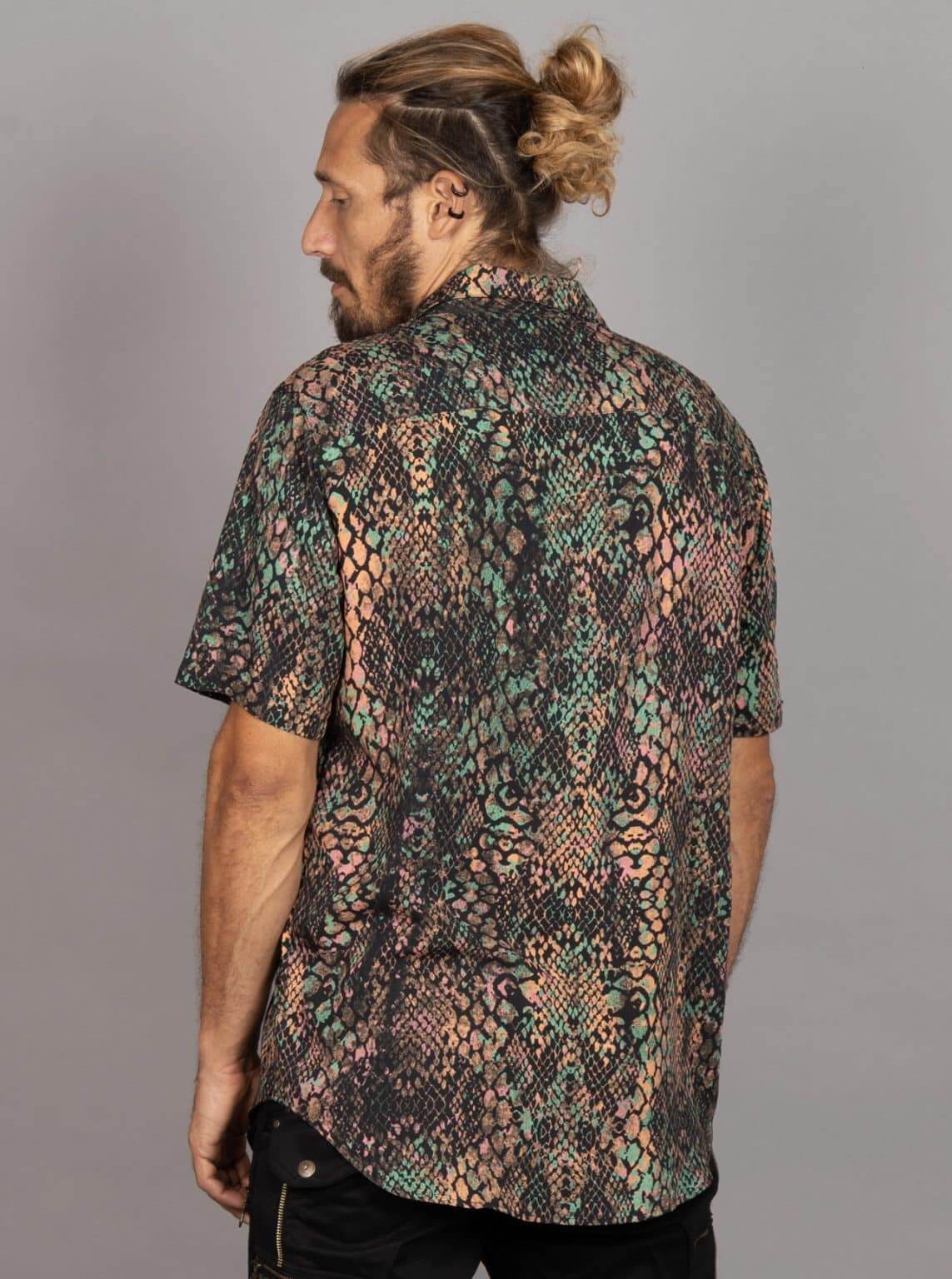 A man wearing a short-sleeve button-up shirt with a complex multicolor snakeskin pattern, shown from a side-back angle against a solid gray studio background.