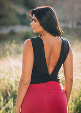 Woman wearing a black sleeveless top with an open back and red pants in a field.