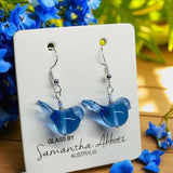 Blue glass bird earrings on a branded card with flowers in the background