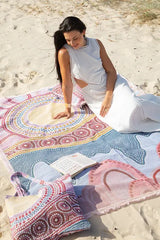 Woman sitting on a colorful beach towel with a book on a sandy beach