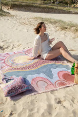 Woman sitting on a colorful beach towel on a sandy beach.