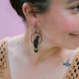 Person wearing a unique earring with a black and green design against a pink background