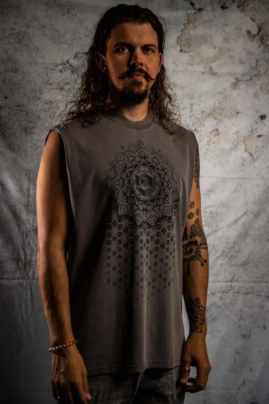 Man wearing a sleeveless shirt with a geometric design against a textured wall.