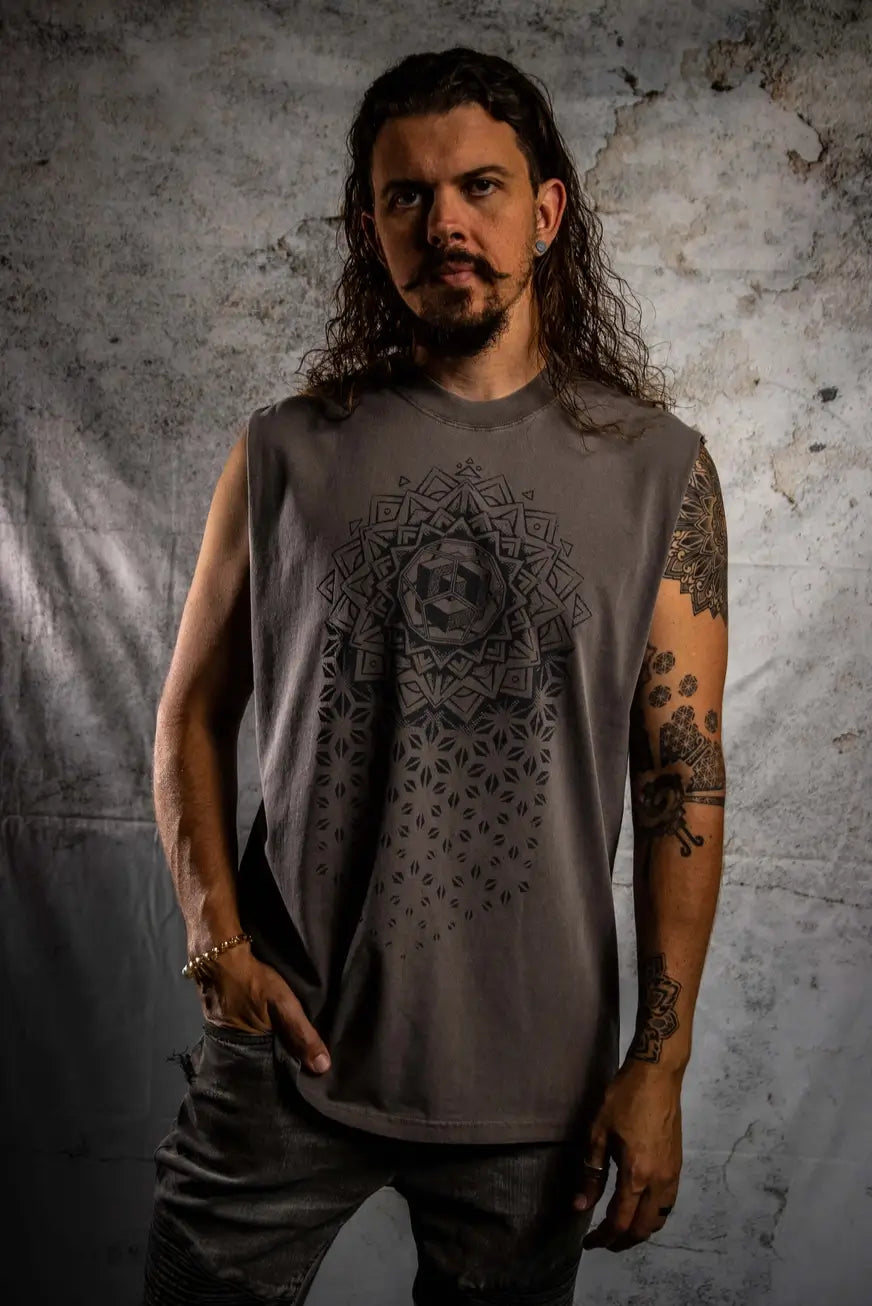 Man wearing a sleeveless gray shirt with a geometric design against a textured wall.