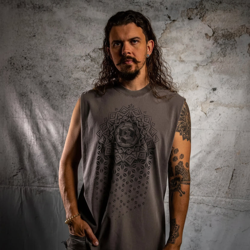 Man wearing a sleeveless gray shirt with a geometric design against a textured wall.