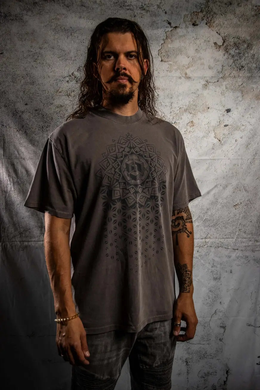 Man wearing a gray t-shirt with a geometric design against a textured wall.