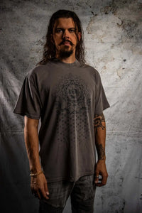 Man wearing a gray t-shirt with a geometric design against a textured wall.