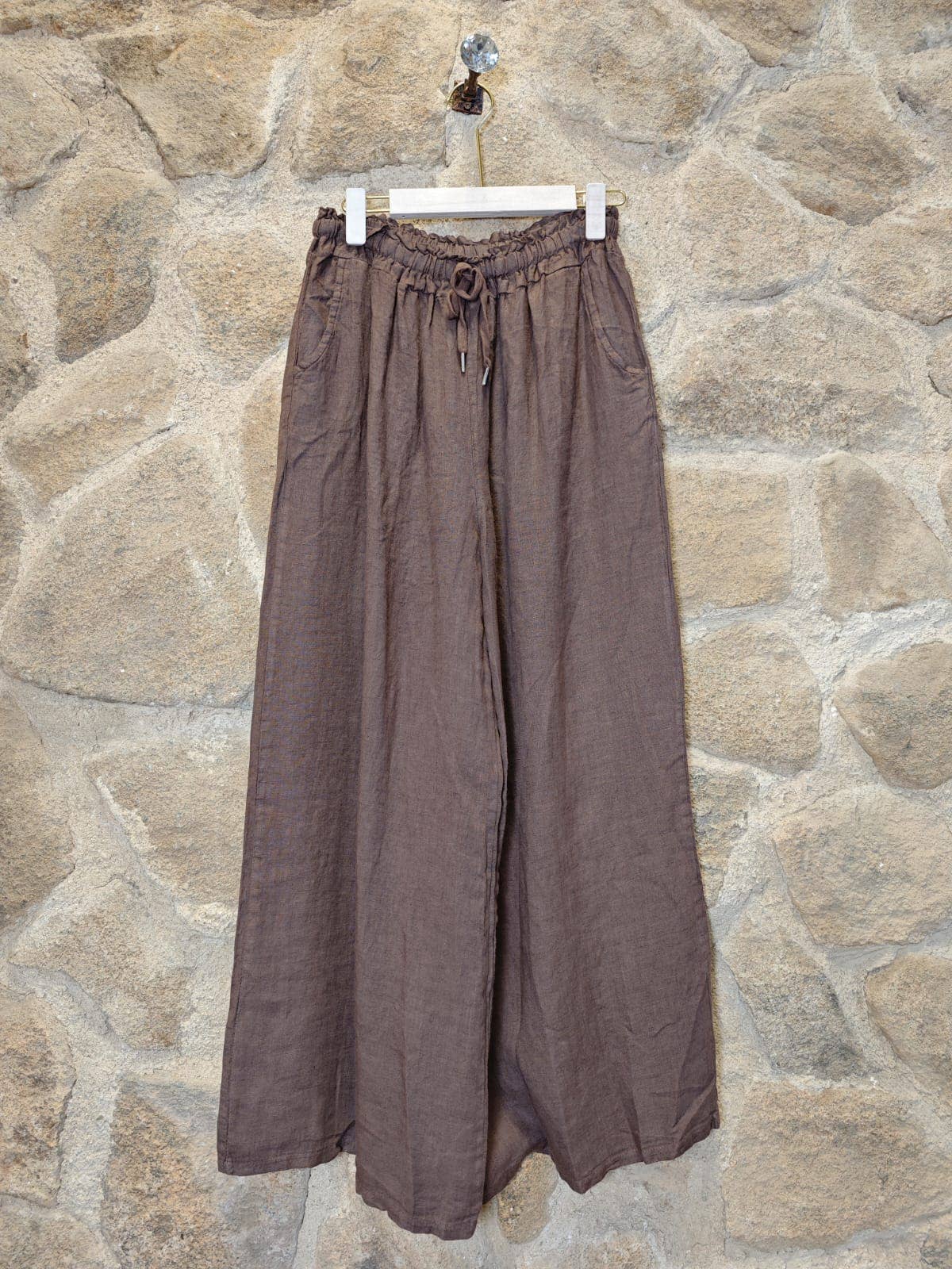 Brown wide-leg pants on a hanger against a stone wall background