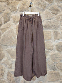 Brown wide-leg pants on a hanger against a stone wall background